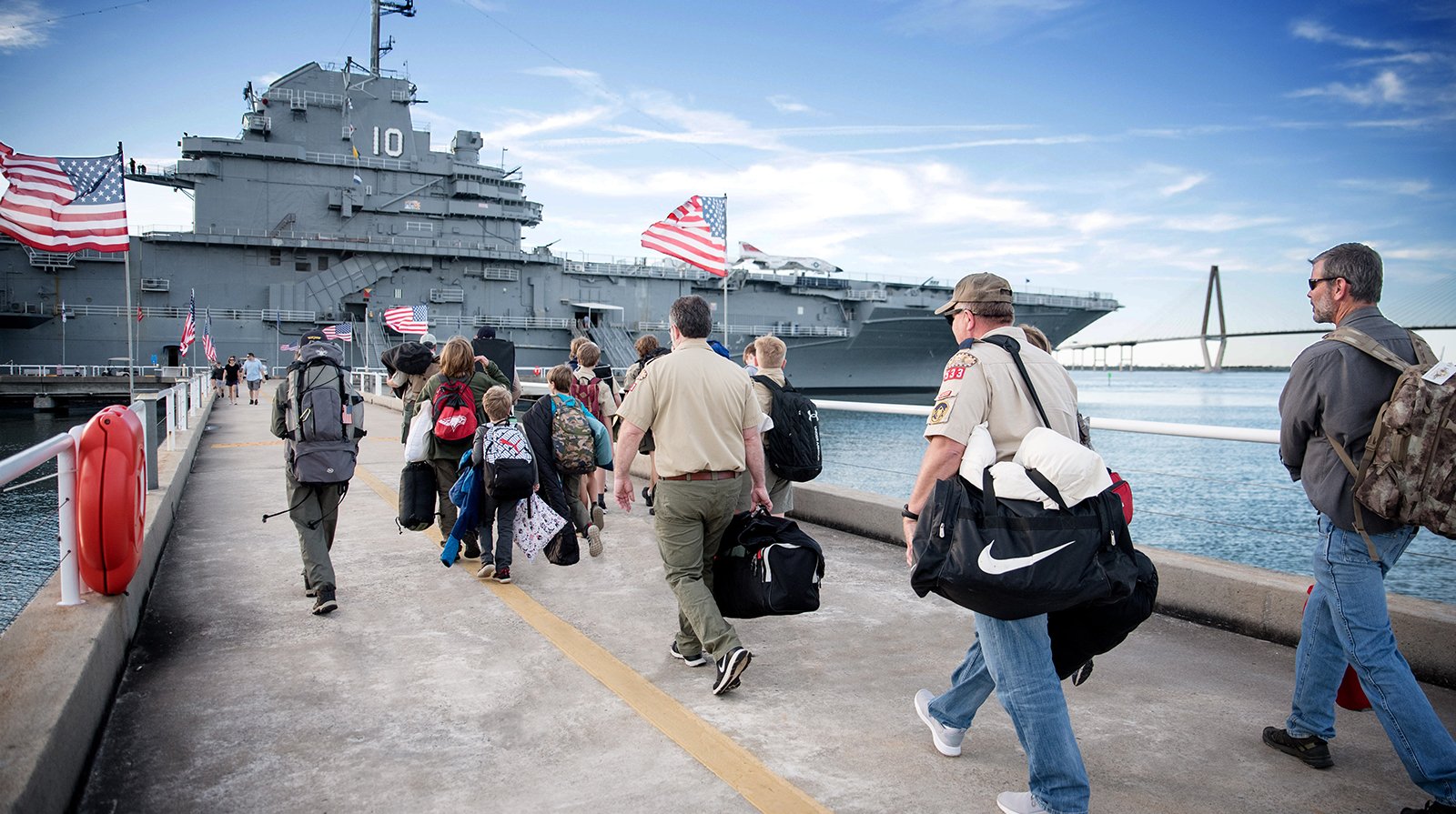 Adults and children walk across the pier leading to the USS Yorktown aircraft carrier to participate in the Operation Overnight camping program.