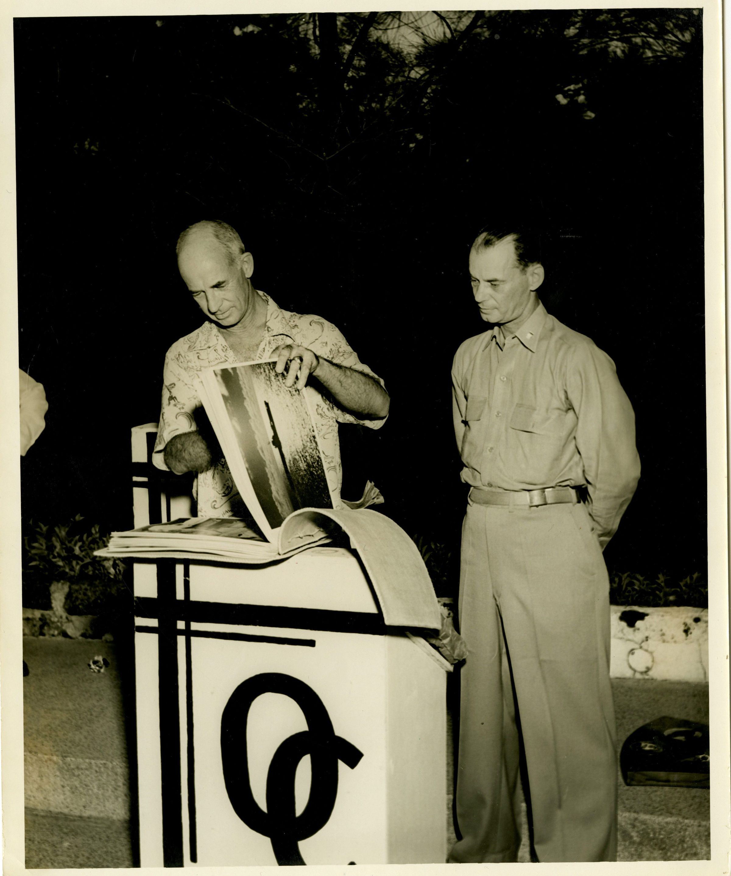 Primary Image of Captain Arnold McKechnie Looking through a Scrapbook at His Farewell Party