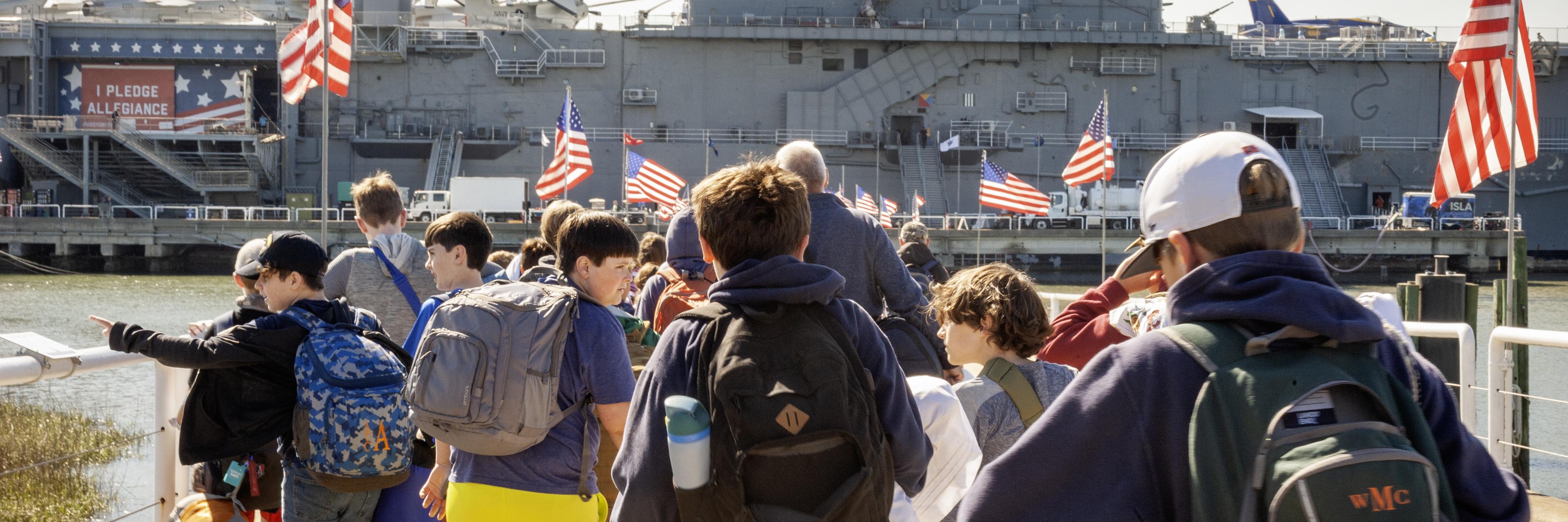 A group of campers walk to the USS Yorktown with their luggage.