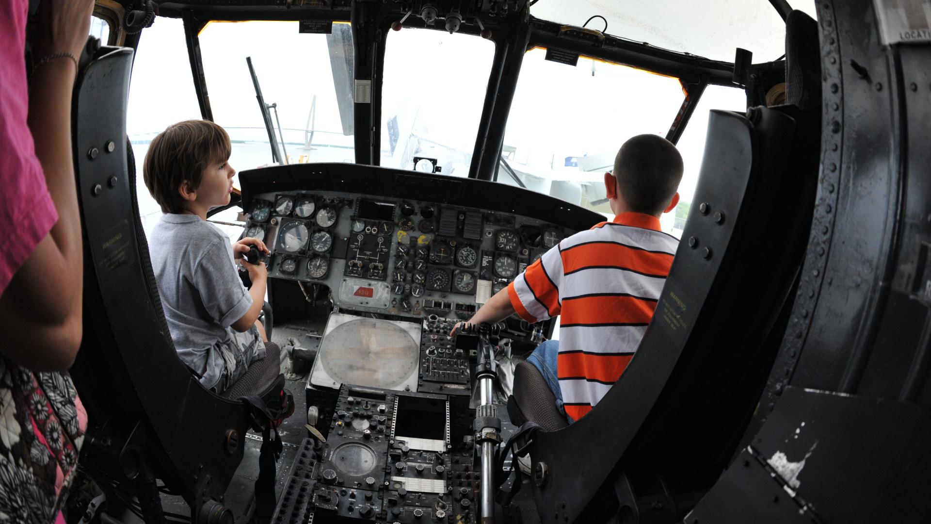 Two boys sit in the front of an aircraft by the controls