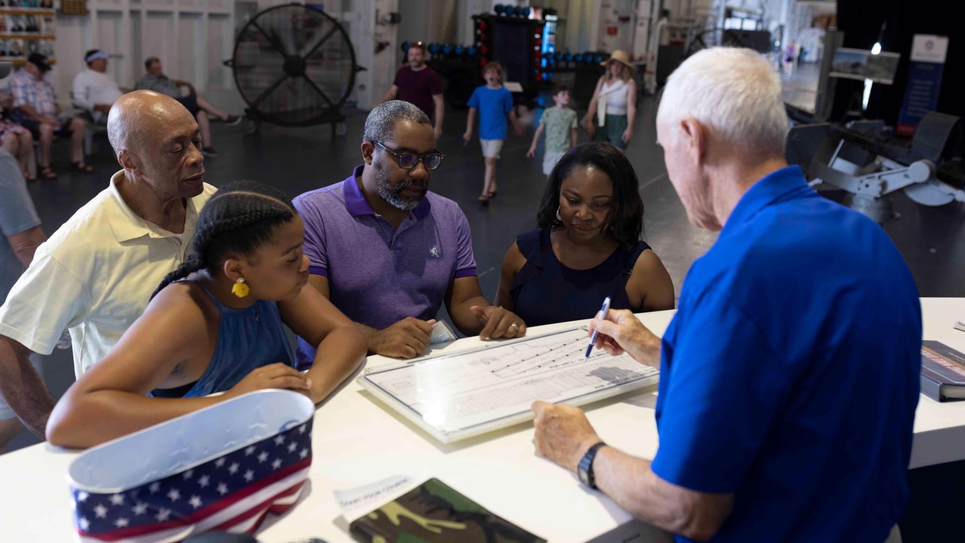 a man at an information desks shows a map of the USS Yorktown to a family