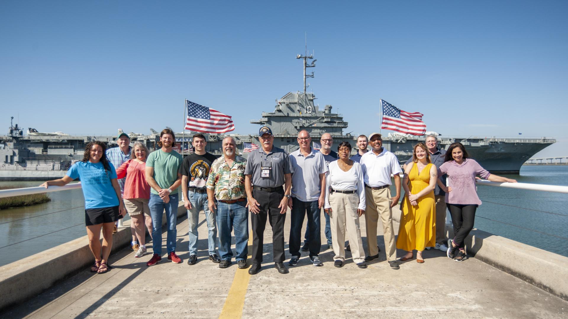 Staff members stand along pier in front of USS Yorktown