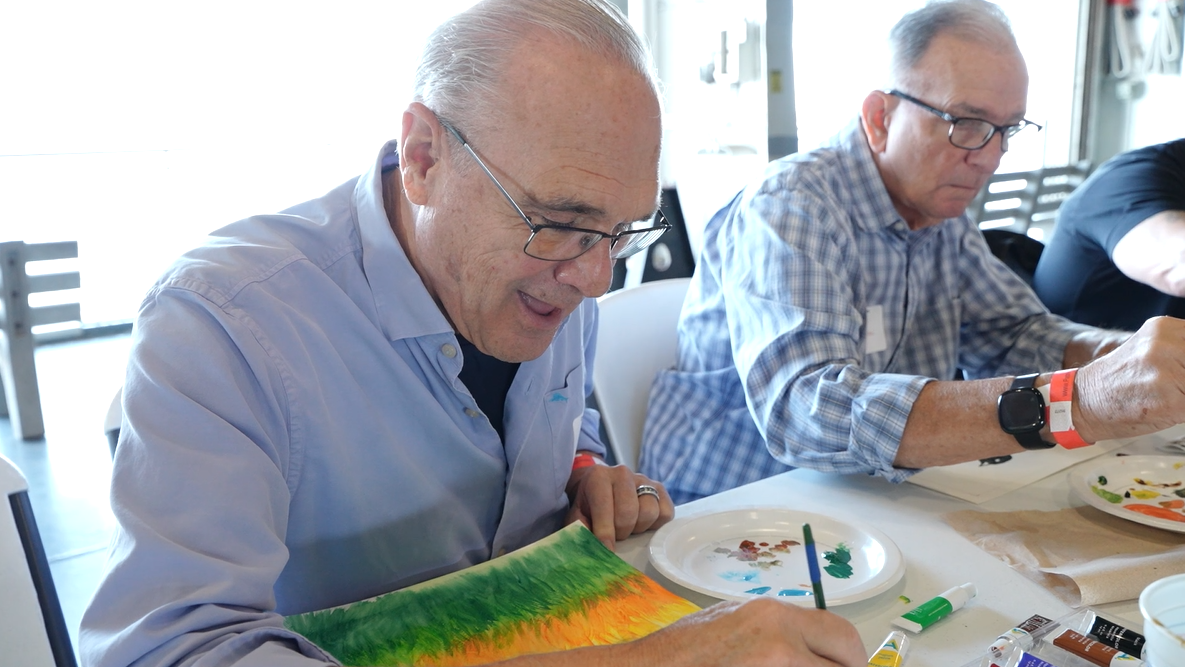 Two veterans sit while painting as they participate in the Patriot Art experience aboard the USS Yorktown (CV-10).