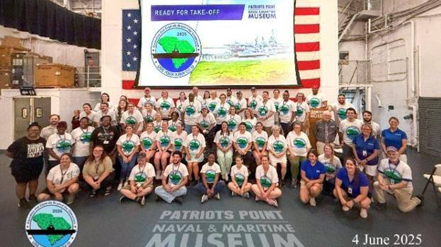 Group of teachers pose for a picture in front of the American flag and a PowerPoint presentation