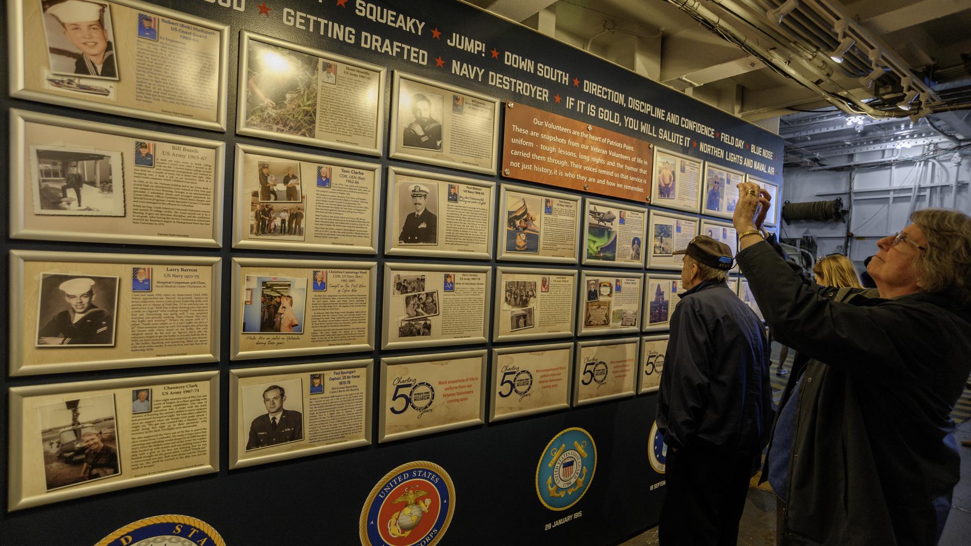 Visitors take photos of the wall featuring framed stories of volunteers' military service.