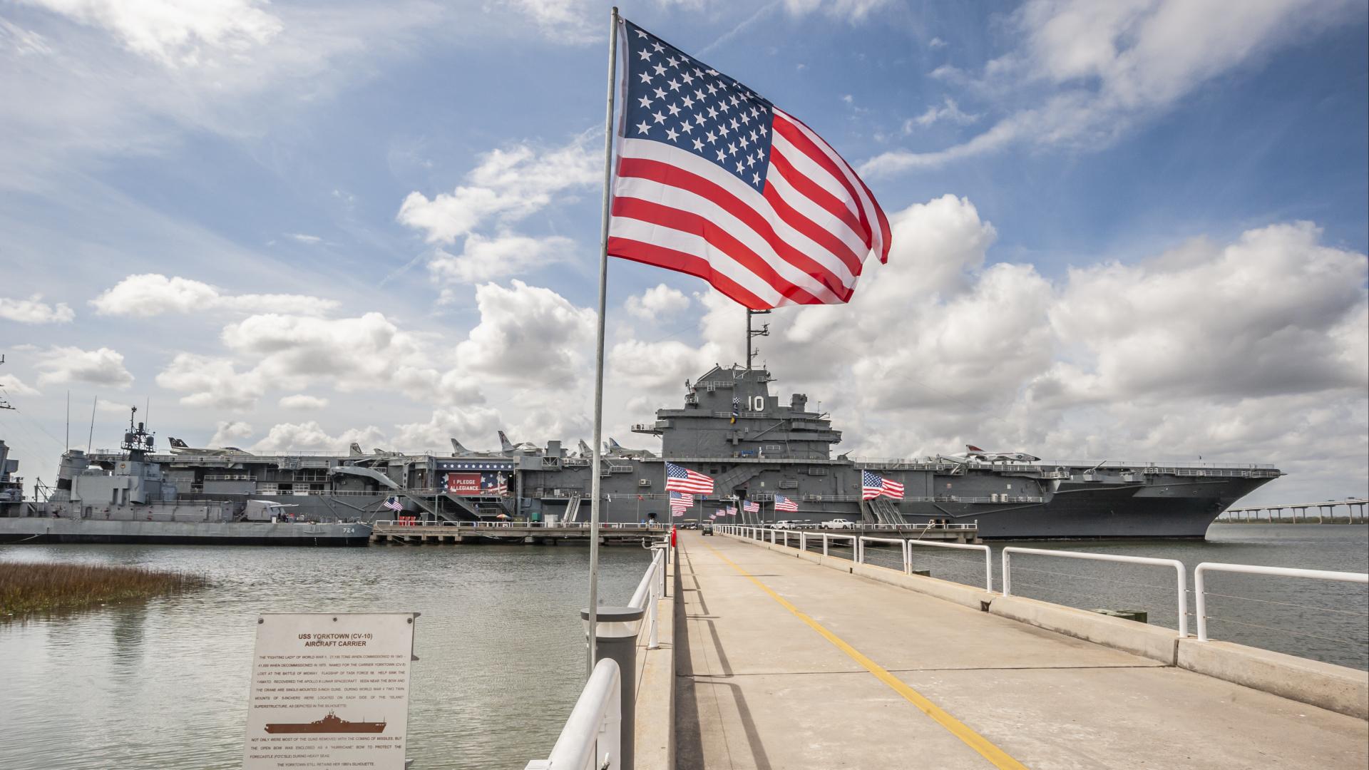 An American Flag waving in the foreground with the USS Yorktown behind.