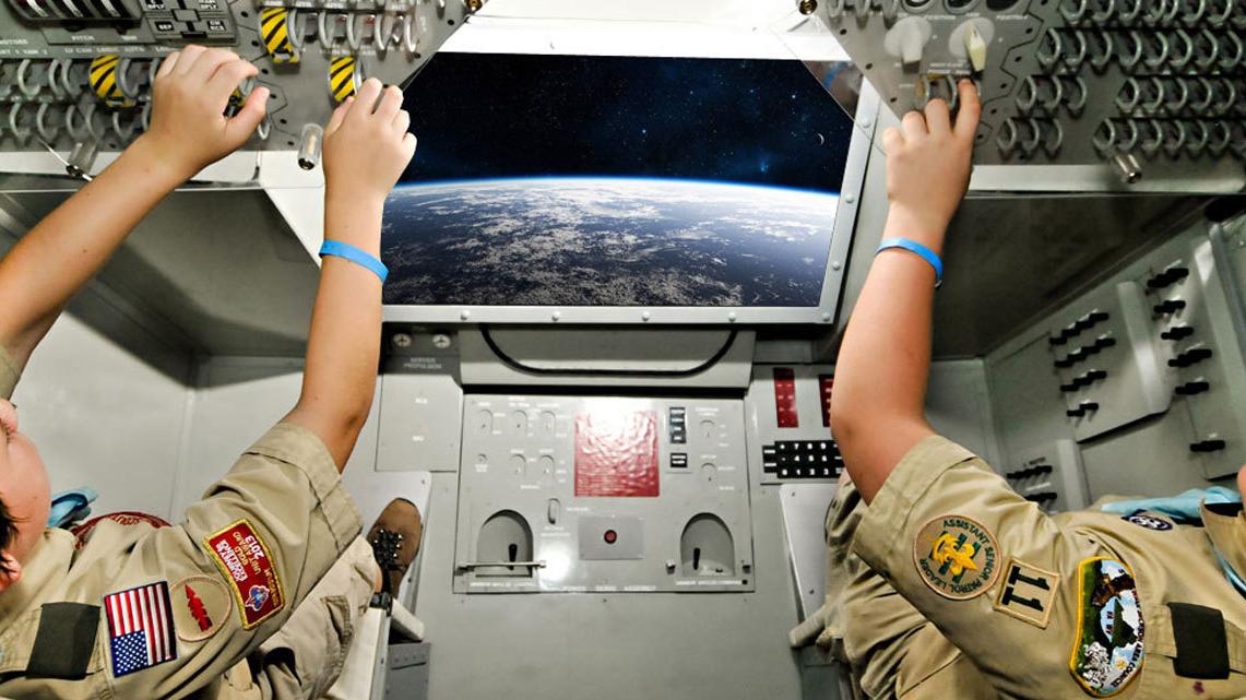 2 boy scouts sit inside the an aircraft simulator