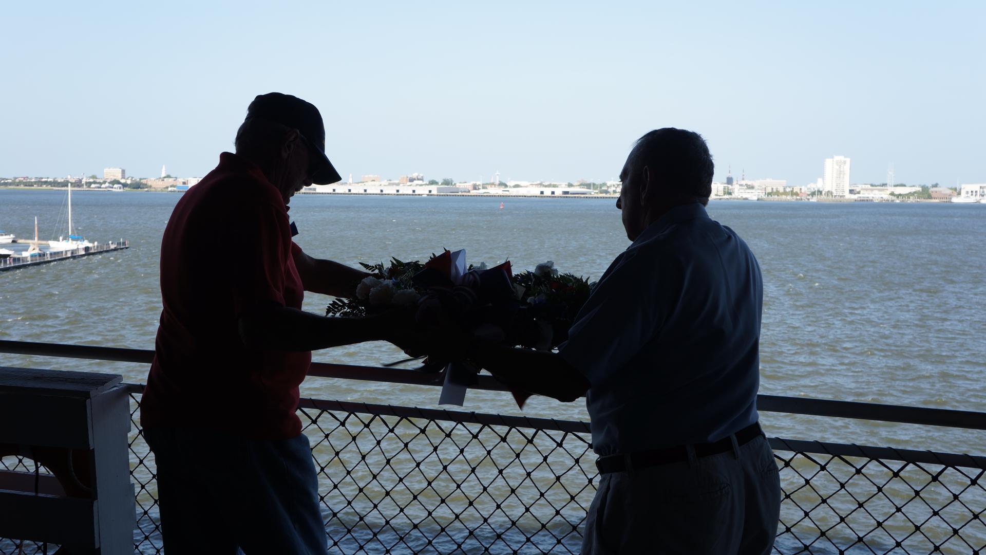 Two men, Tin Can Sailors hang a memorial wreath during the annual reunion