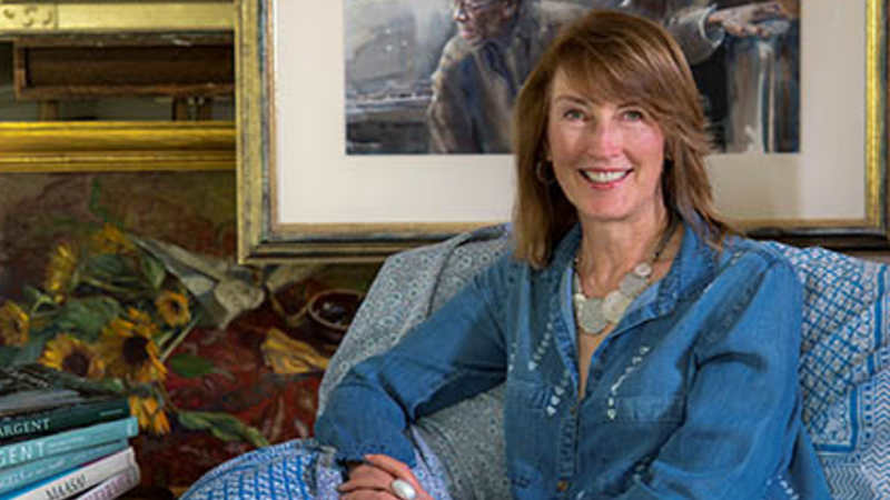 Female with shoulder length brown hair sits in front of some paintings