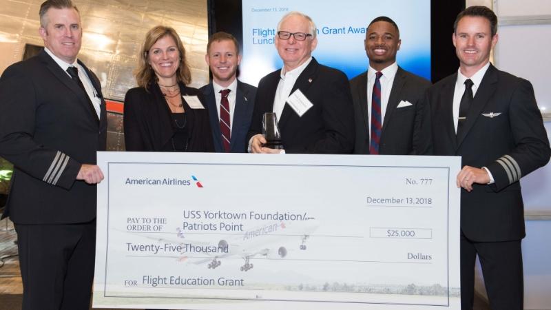 Six individual stand holding a large check made out to the USS Yorktown Foundation for 25,000