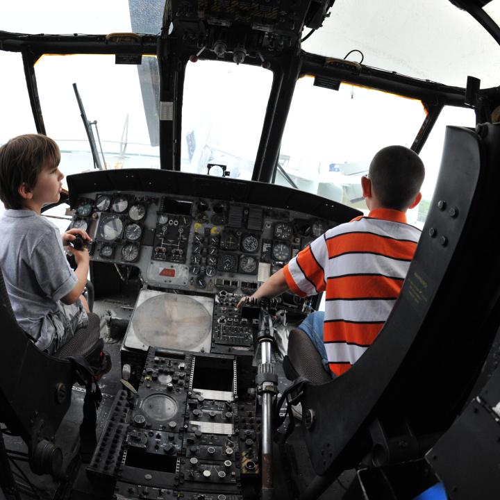 Two boys sit in the front of an aircraft by the controls