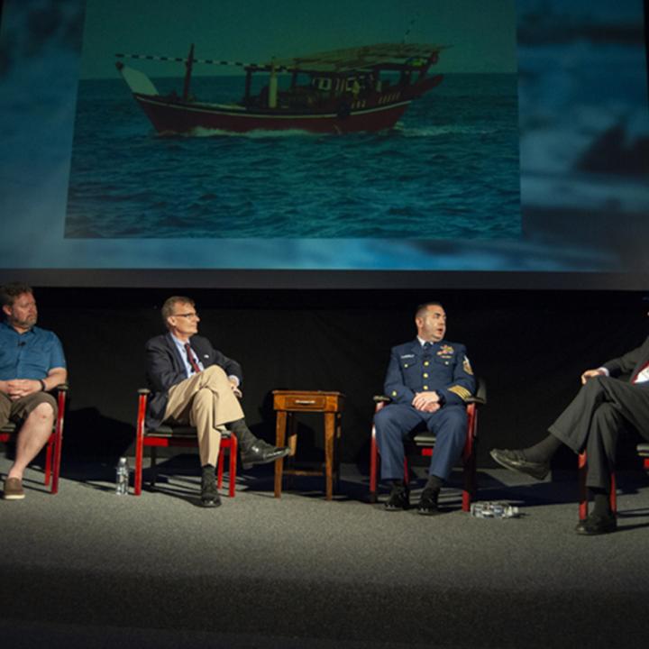 Four men seated speaking at a symposium