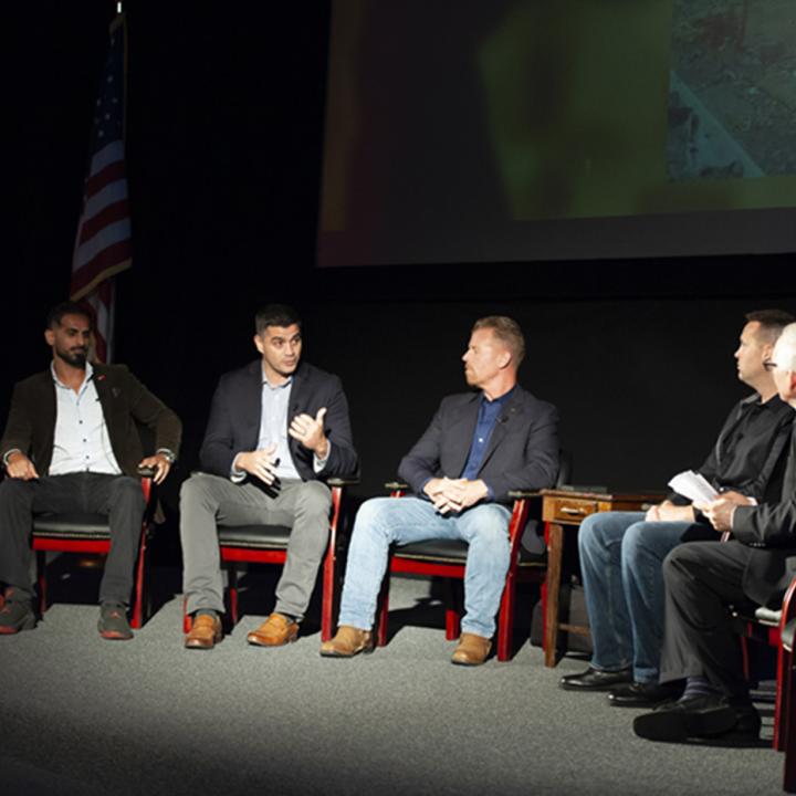 Five men seated speaking at a symposium