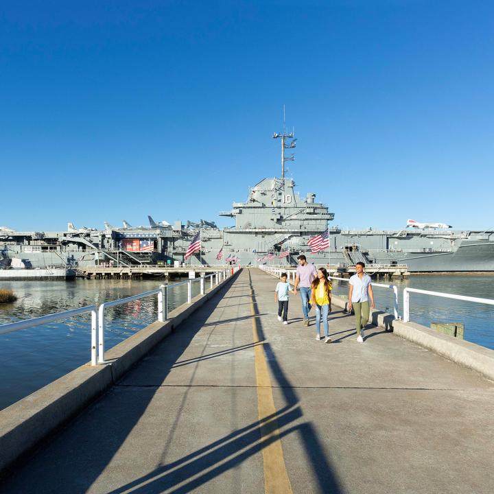 A family of four walking on a bridge away from the USS Yorktown aircraft carrier.