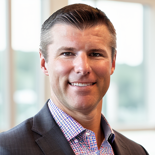 A man with slicked back hair in a button up patterned shirt and suit coat