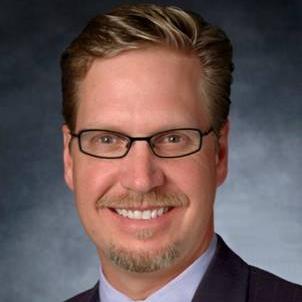 A man with blond hair, mustache and some beard with glasses in a suit and tie