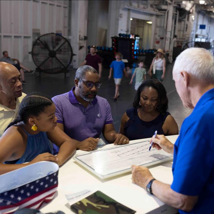 a man at an information desks shows a map of the USS Yorktown to a family