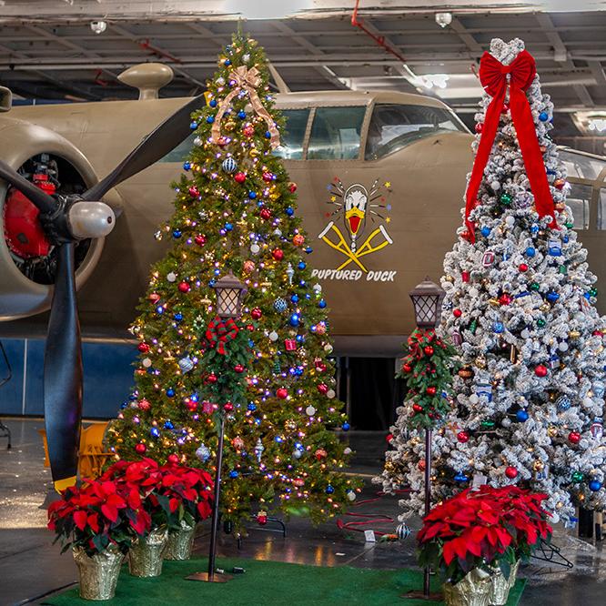 Two Christmas trees decorated with lights in front of an aircraft