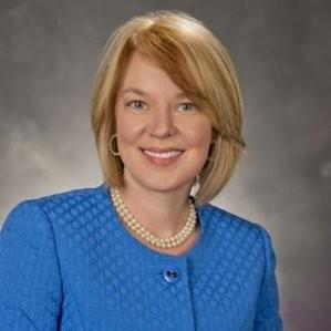 Woman with shorter blond hair wearing a double strand of pearls and a blue coat