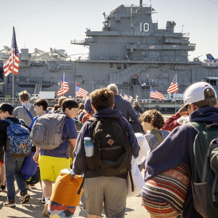 A group of campers walk to the USS Yorktown with their luggage.