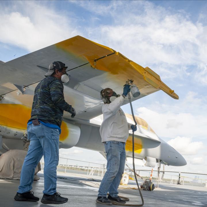Two men repainting the wings of an aircraft