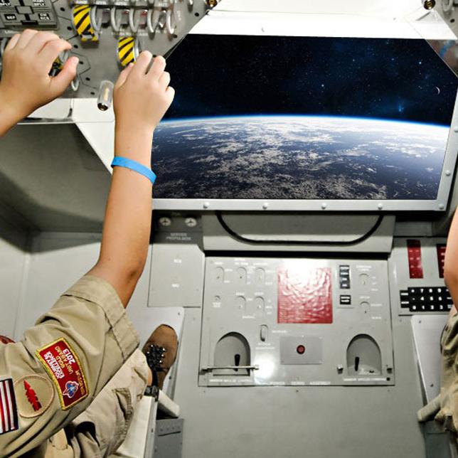 2 boy scouts sit inside the an aircraft simulator