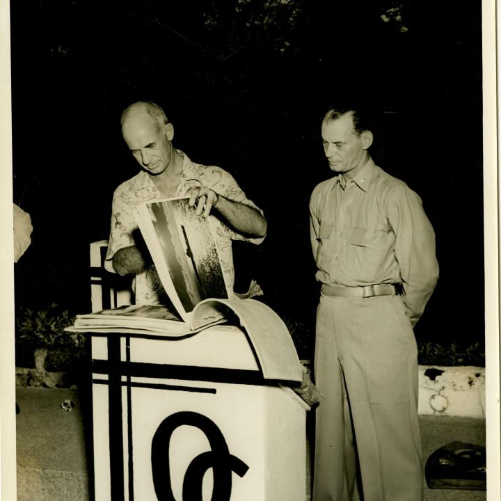 Primary Image of Captain Arnold McKechnie Looking through a Scrapbook at His Farewell Party