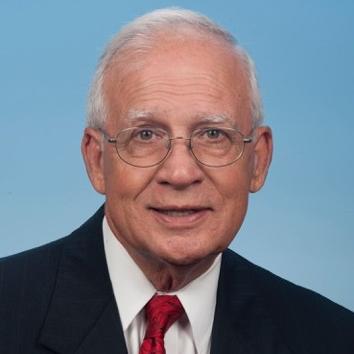 Portrait of an older man with grey hair and glasses in a suit with a red tie