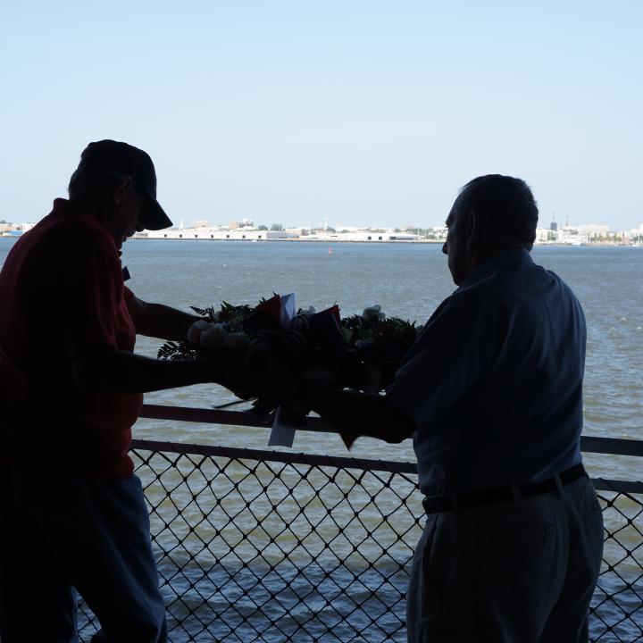 Two men, Tin Can Sailors hang a memorial wreath during the annual reunion