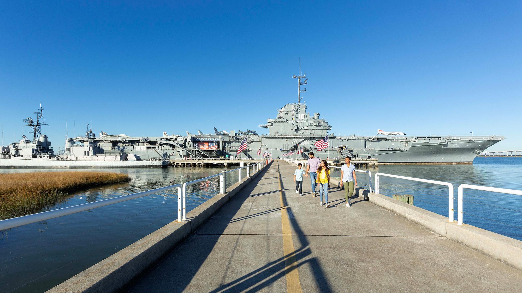 A family of four walking on a bridge away from the USS Yorktown aircraft carrier.