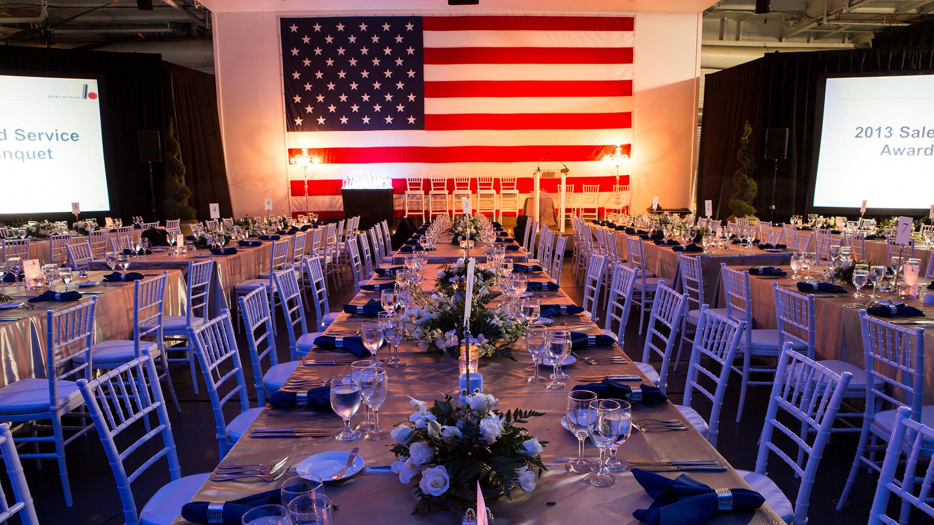 Long tables set up in the Hangar Bay with flowers for center pieces