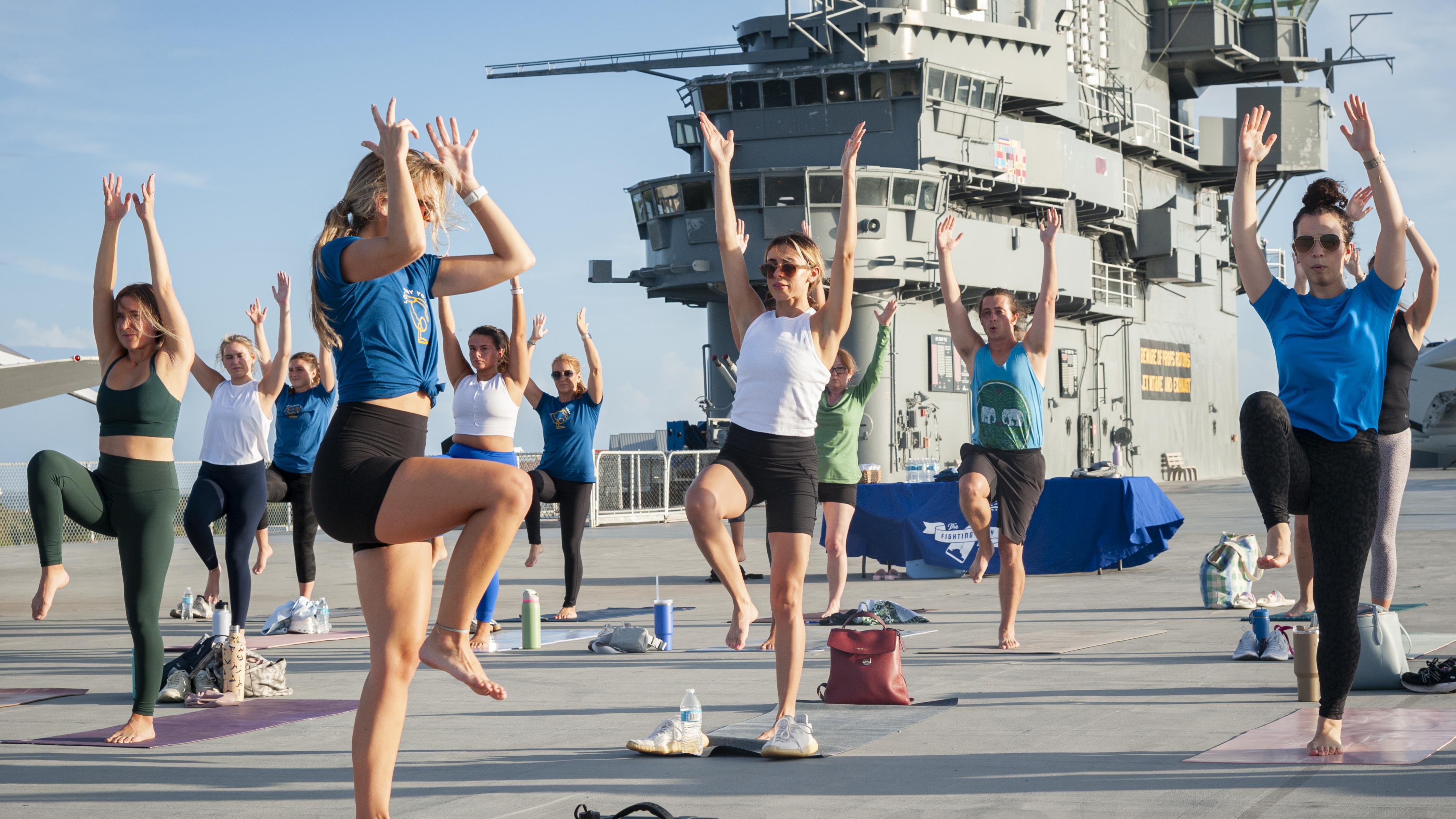 A group of people doing yoga on the flight deck of an aircraft carrier.