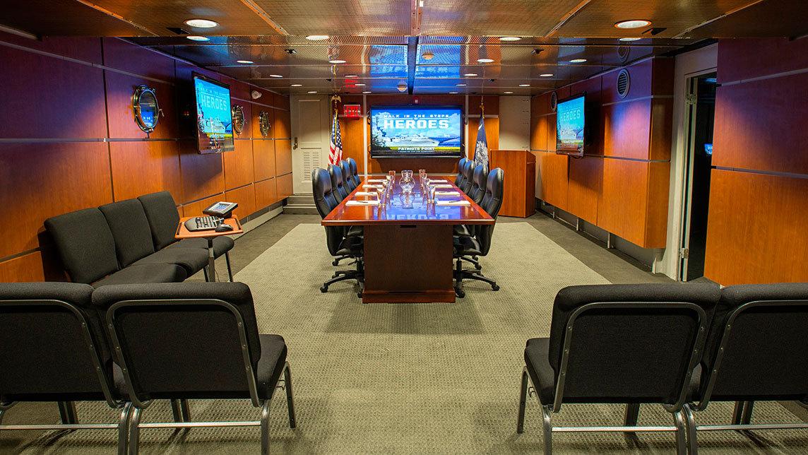 image of a board room with a large table in the center surrounded by chairs and wall mounted monitors