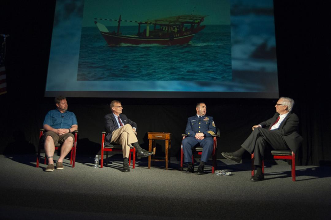 Four men seated speaking at a symposium