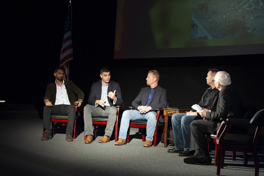 Five men seated speaking at a symposium