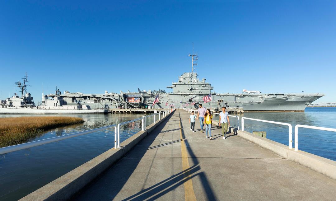 A family of four walking on a bridge away from the USS Yorktown aircraft carrier.