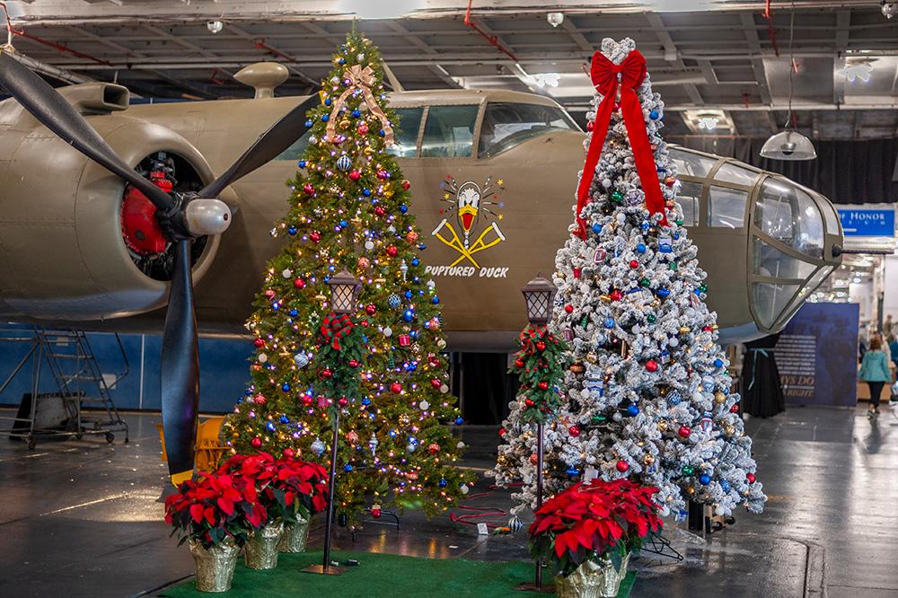Two Christmas trees decorated with lights in front of an aircraft