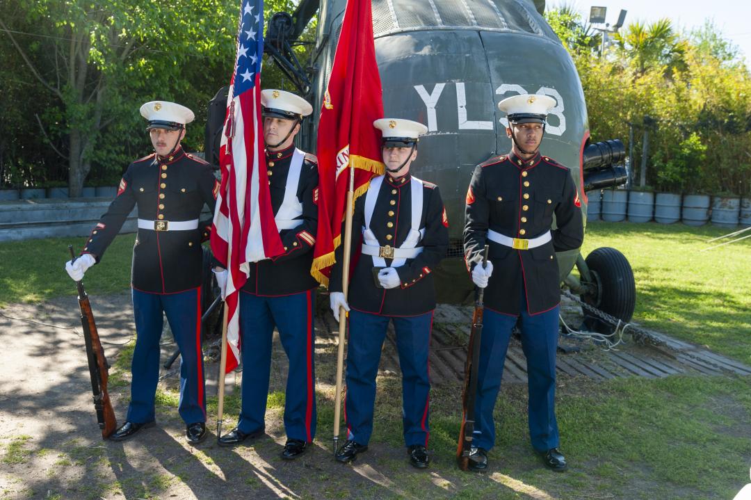 Honor guards salute in front of a Vietnam-era helicopter during a Vietnam Veterans Day event.