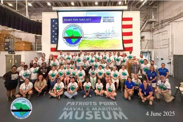 Group of teachers pose for a picture in front of the American flag and a PowerPoint presentation