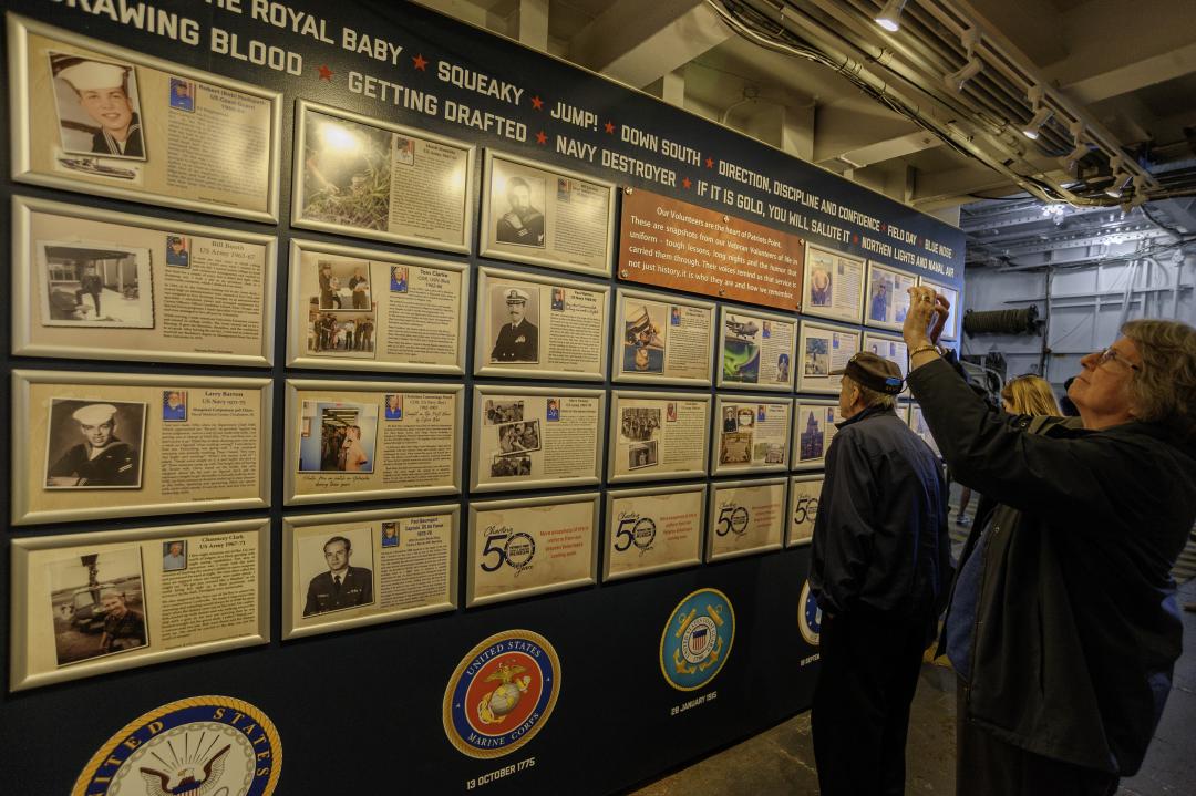 Visitors take photos of the wall featuring framed stories of volunteers' military service.