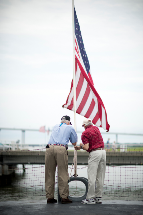 Two men tie up a flag at the bow of the USS Laffey. 